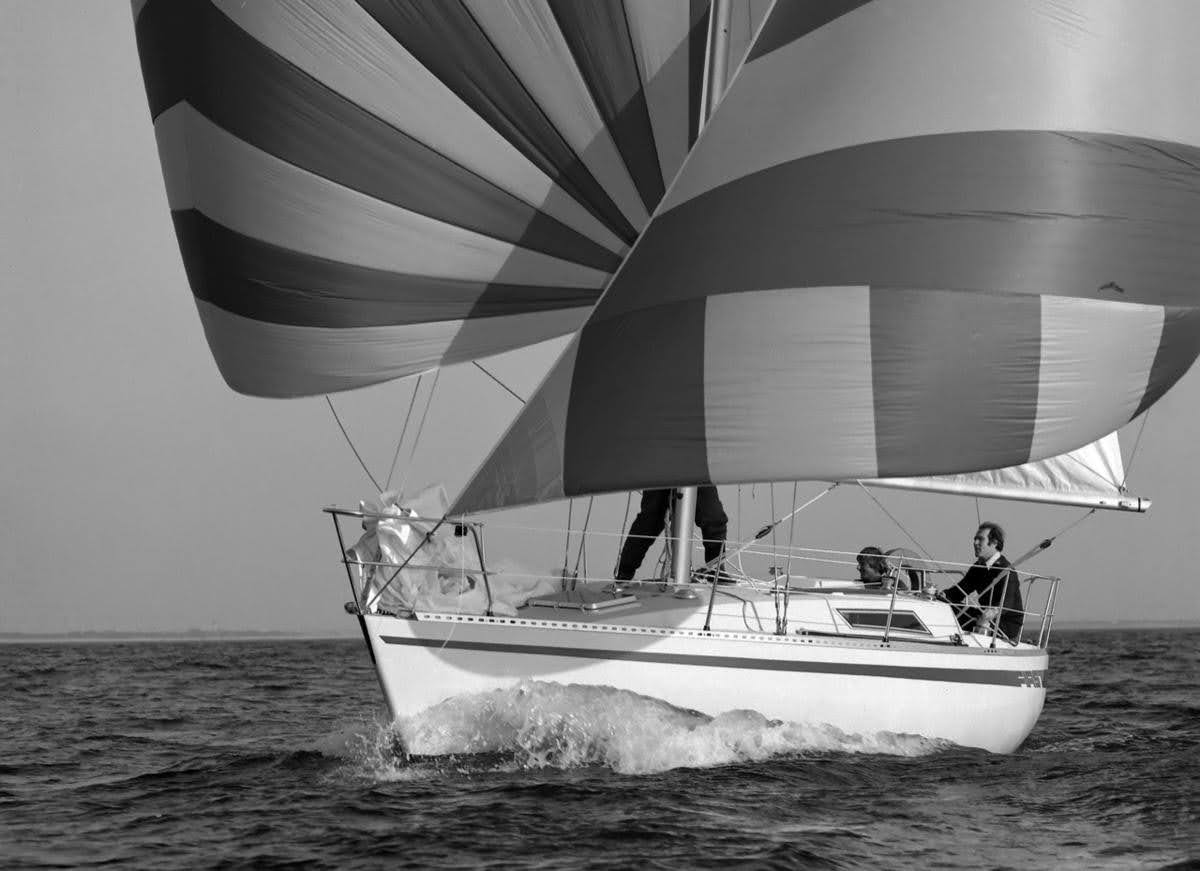 A black and white image of the "First 30" with striped sails speeds across the sea. 