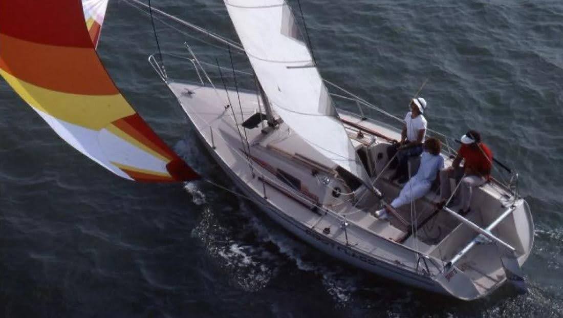 Three people sit aboard a First Class 8 with colourful sails on the open sea.