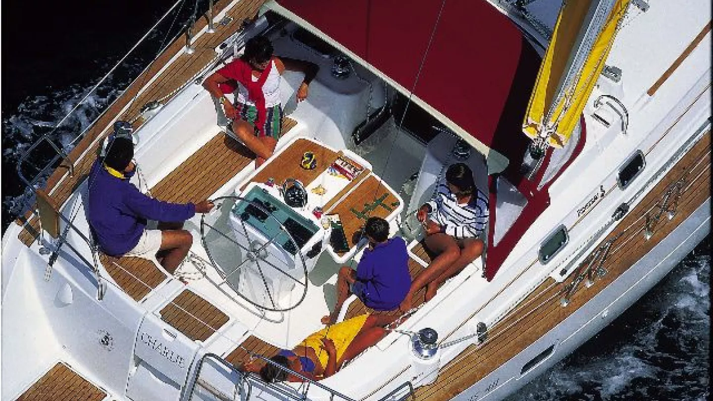 A man steers an Océanis 411 Clipper, while three other people sit on the deck as they sail in the sun