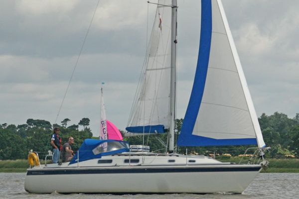 Three people on board a white Westerly Fulmar with white and blue sails.