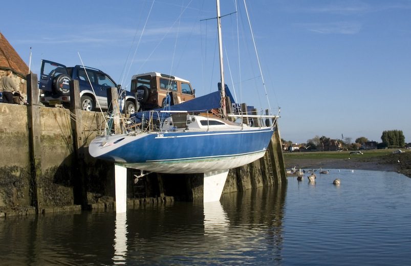 A blue and white fin-keeled sailing yacht tied to a harbour wall, having dried out for maintenance work mid-season.