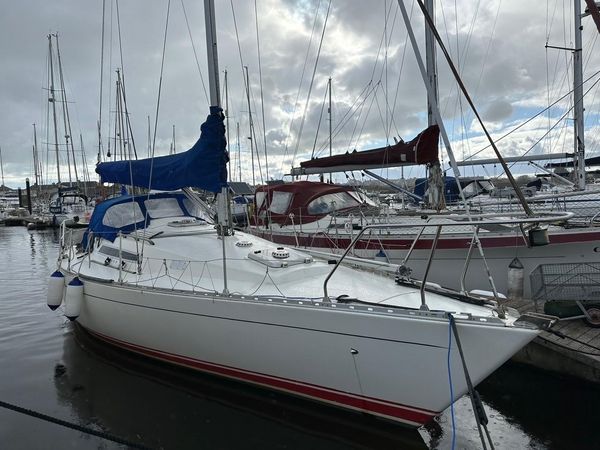 A white Sigma 33 with a blue sail is moored in Pwllheli, Wales.