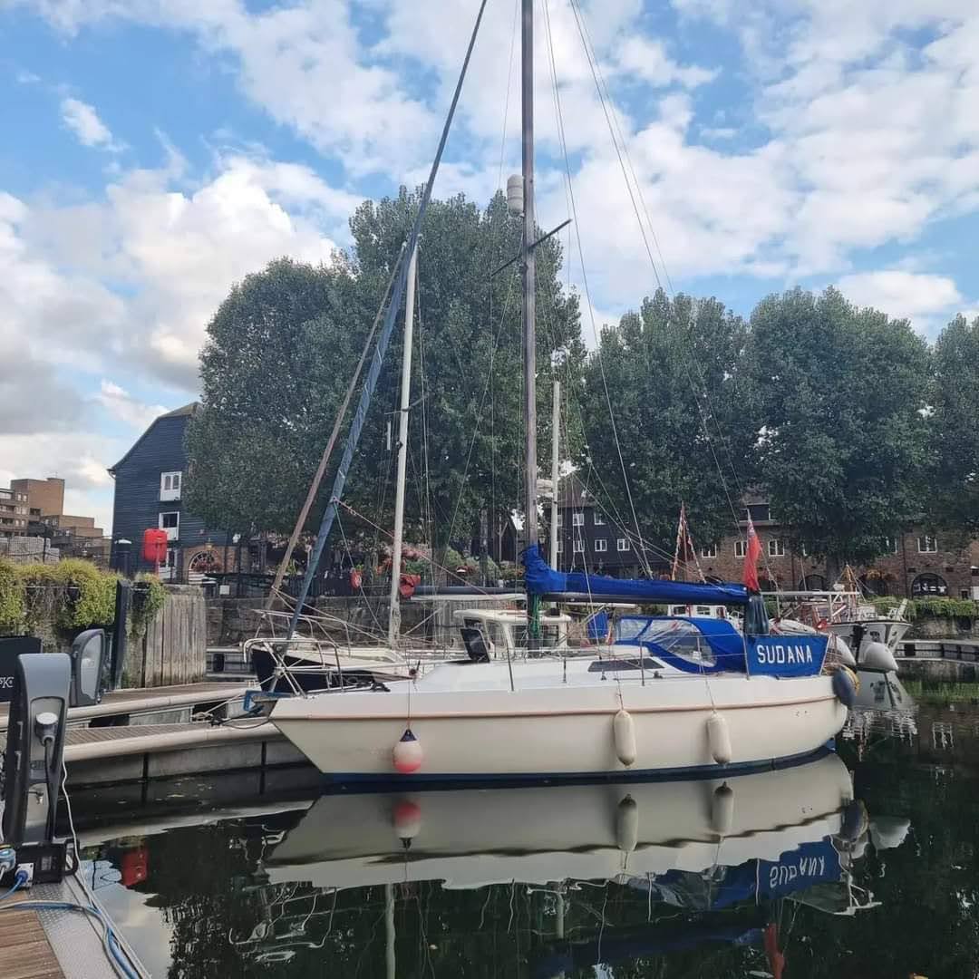 A white and blue Thames Mirage sailing boat named Sudana moored in St Katharine's docks, London