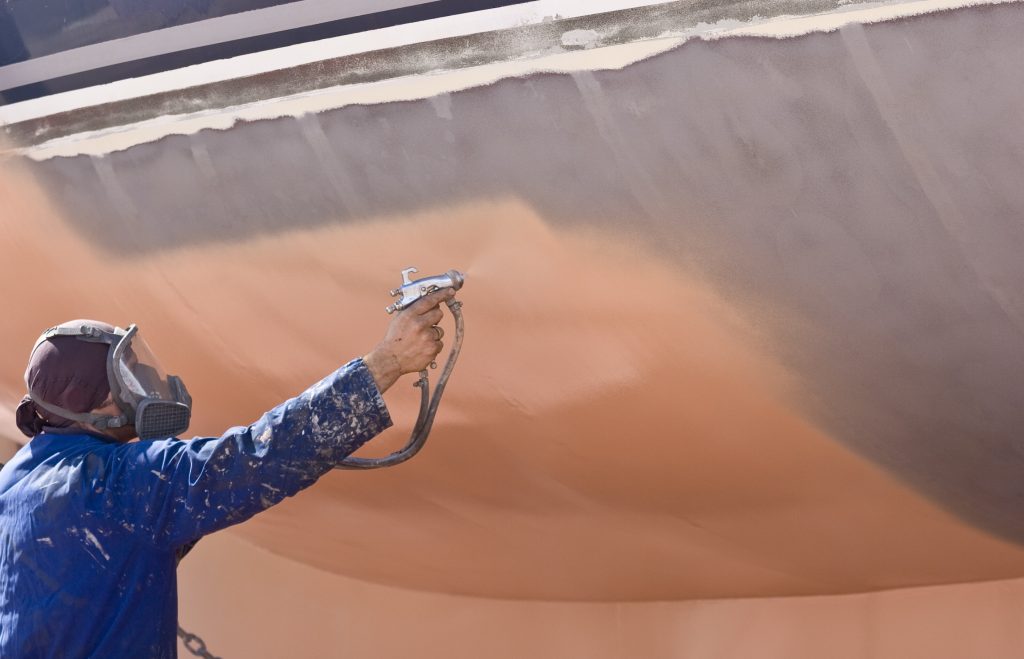 Spray painter with full body protection and mask painting the hull of sailboat